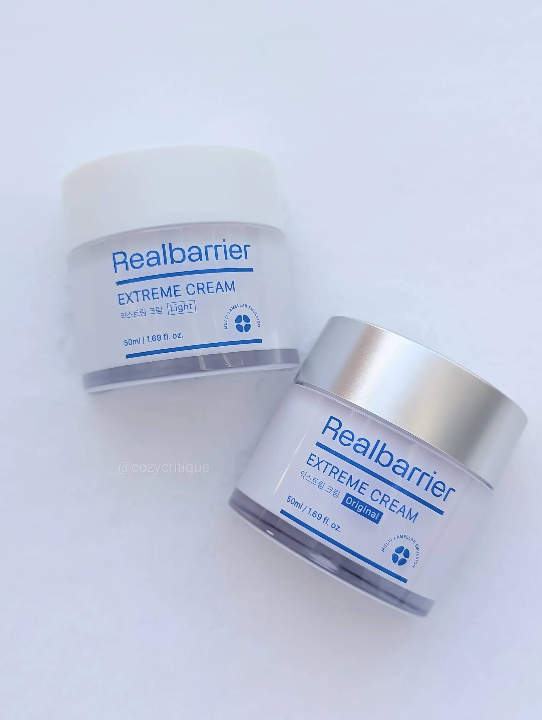 Two jars of Real Barrier Extreme Cream, labeled "Light" and "Original," on a snowy surface. Silver and white lids, minimal design.