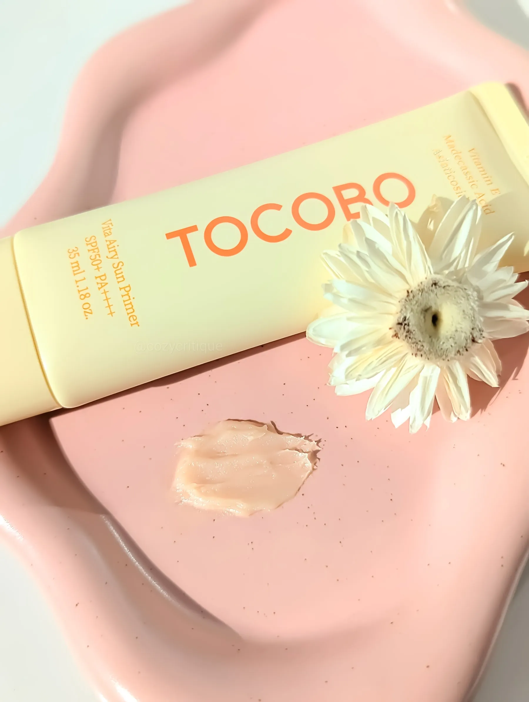 Tube labeled "TOCOBO" on pink tray with daisy and cream smear. Soft, pastel colors create a calm, fresh mood.